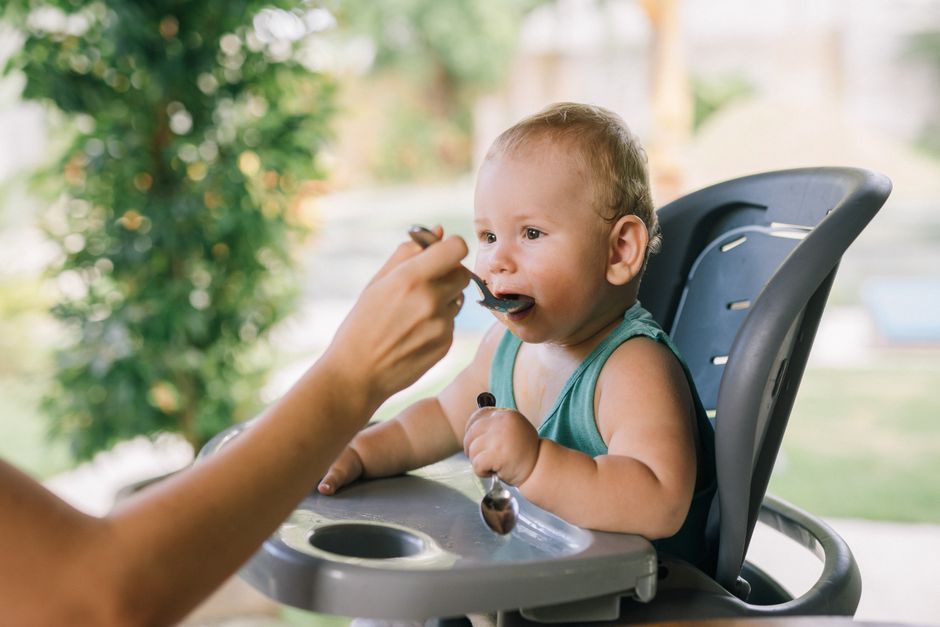 Cute baby eating with a spoon in a high chair outdoors