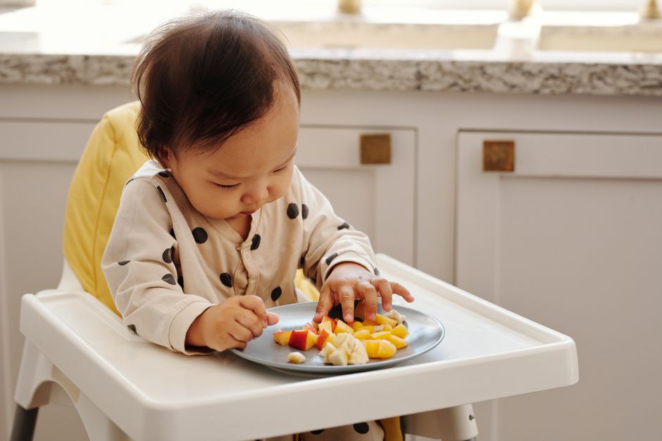A baby happily tasting fresh fruit in a supportive high chair