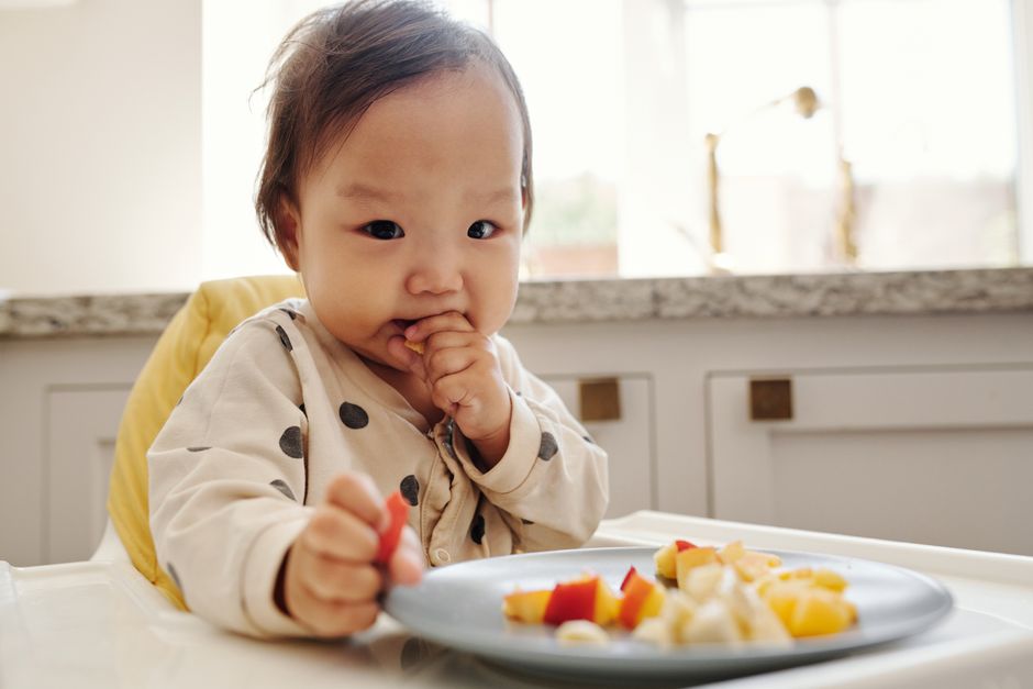 Cute toddler enjoying fresh fruit slices in high chair