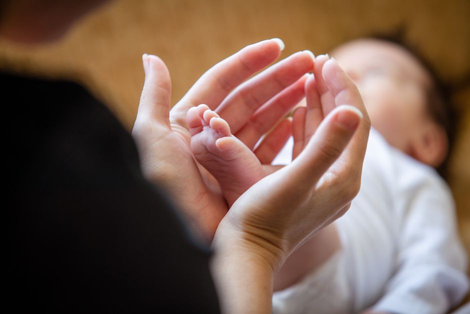 Mother's hands gently holding newborn's feet with warmth