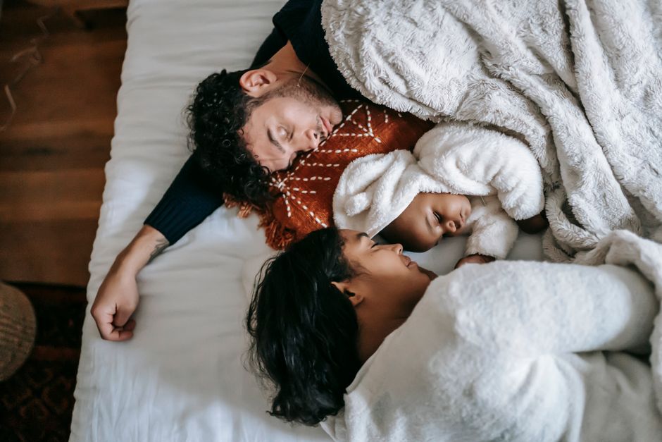 Top view of happy young multiethnic family with adorable newborn baby lying and sleeping on comfortable bed