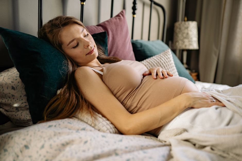 A serene pregnant woman resting in bed, showcasing relaxation and comfort