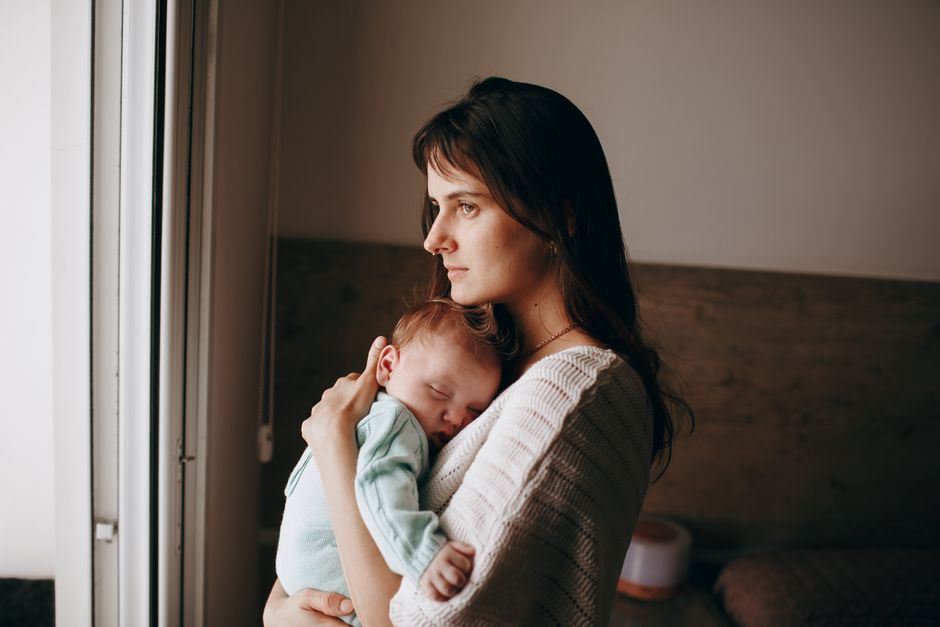 A mother holding her baby in a quiet room reflecting on postpartum recovery
