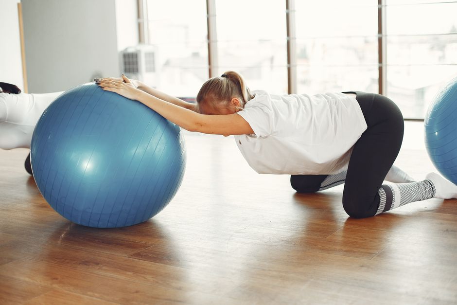 Side view of female sportswoman while group training with fitness ball during prenatal workout with crop friend in modern gym during daytime