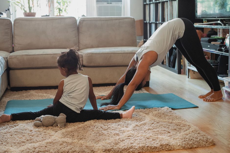 Unrecognizable female and little girl in sportswear stretching on carpet and stretch mat in living room