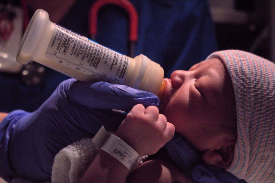 A mother safely feeding an infant with a milk bottle in a calm nursery