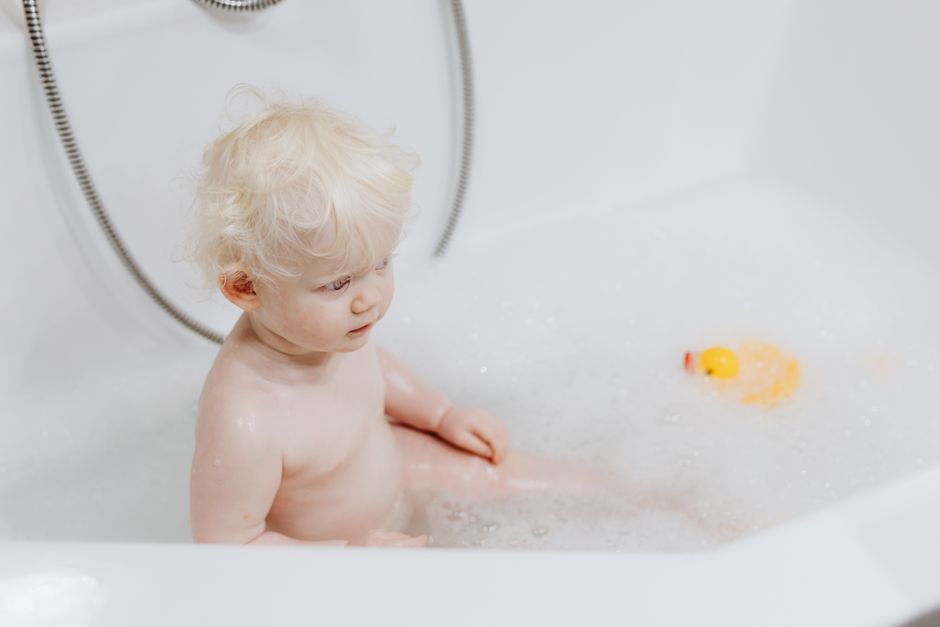 Cute blonde baby enjoying a bubble bath with a rubber duck in a clean bathtub