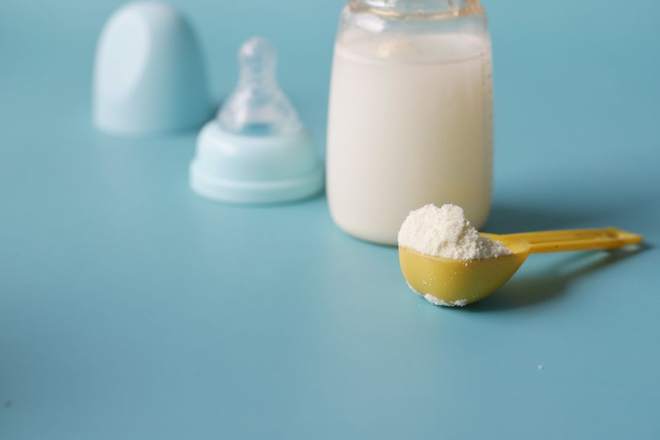 Close-up of baby milk formula powder in a measuring scoop next to a prepared bottle