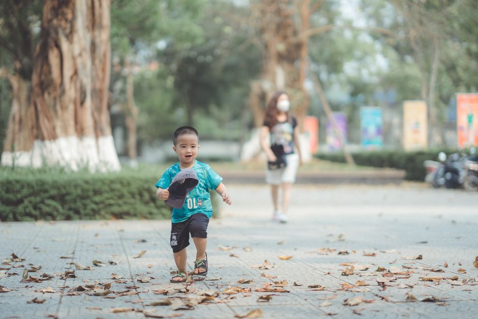 Asian boy in a blue shirt joyfully running in a sunlit park during daytime