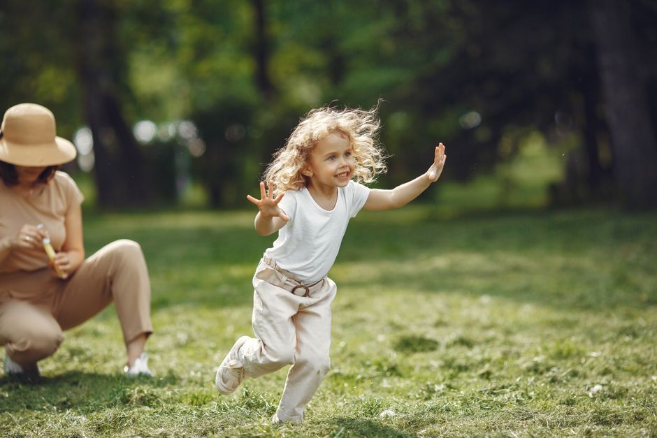 A carefree child with curly hair runs happily on the grass in a sunlit park