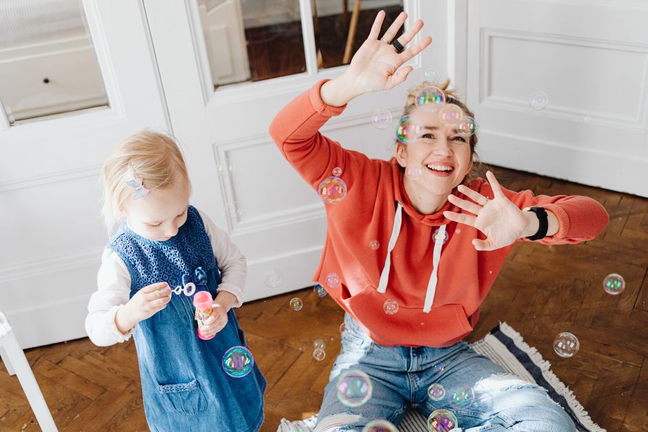 Joyful scene of a woman and child playing with bubbles indoors, capturing laughter and fun