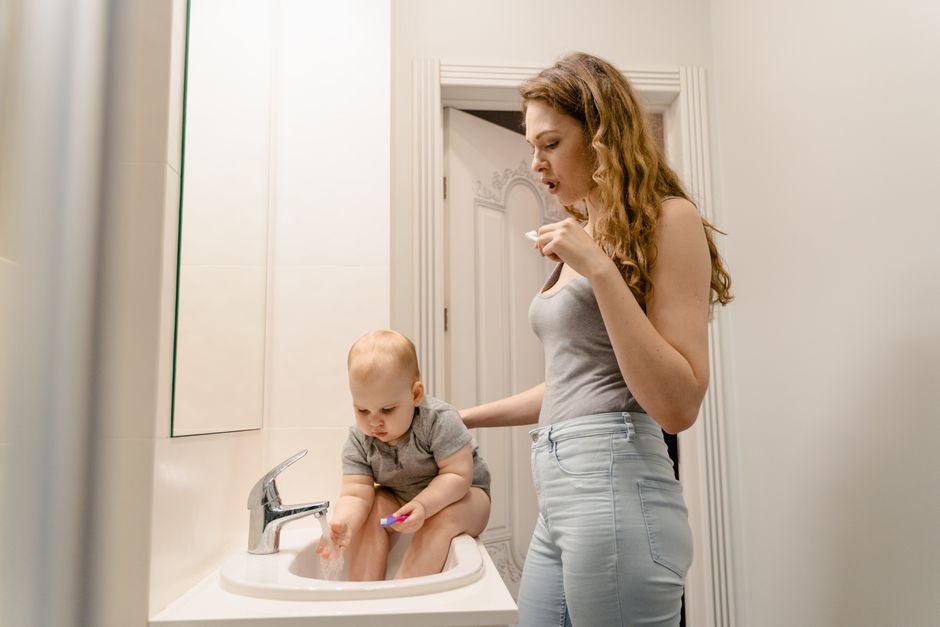 Mother and toddler bonding joyfully while brushing teeth together in front of bathroom mirror