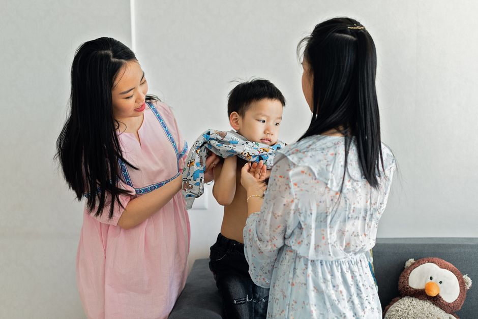 Parents helping child dress on cozy couch