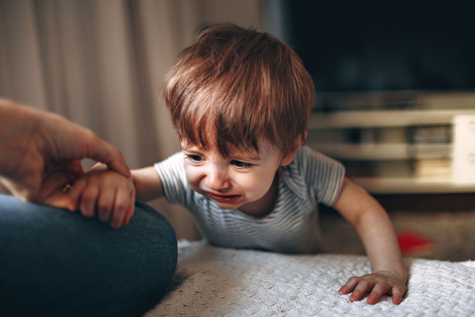 Parent soothing upset toddler gently on living room couch