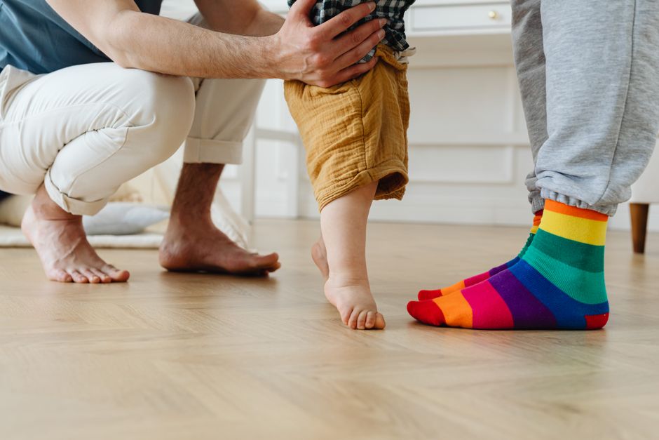 Loving parent helping a toddler take steady barefoot steps across an indoor living room floor