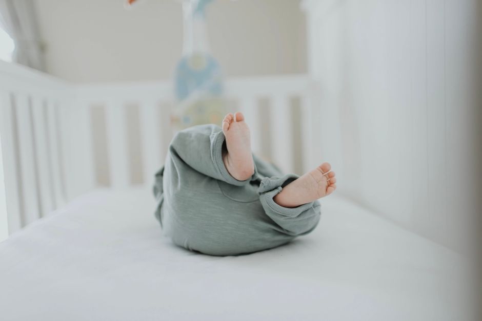 Cute baby feet in pajamas on a soft white crib