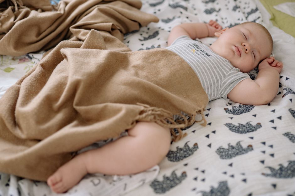 A serene baby sleeping on a patterned blanket, wrapped in a warm brown cover