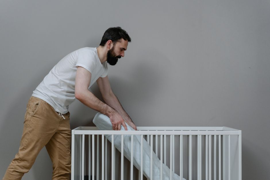 Father carefully assembling a safe, minimalist crib with a firm flat mattress in nursery