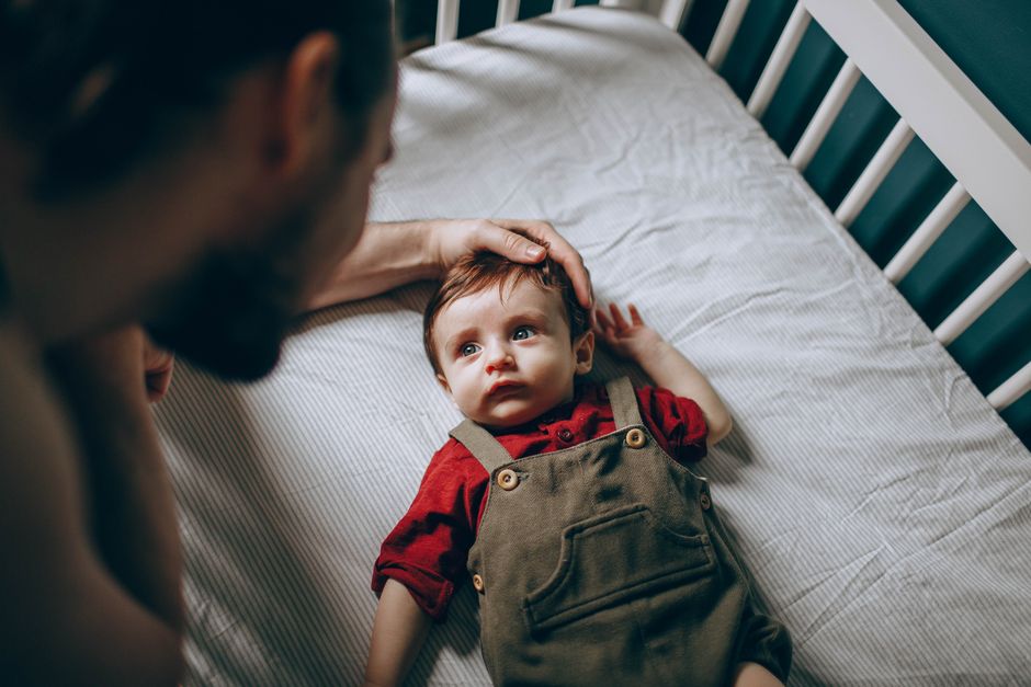 Father comforting baby safely in bare wooden crib