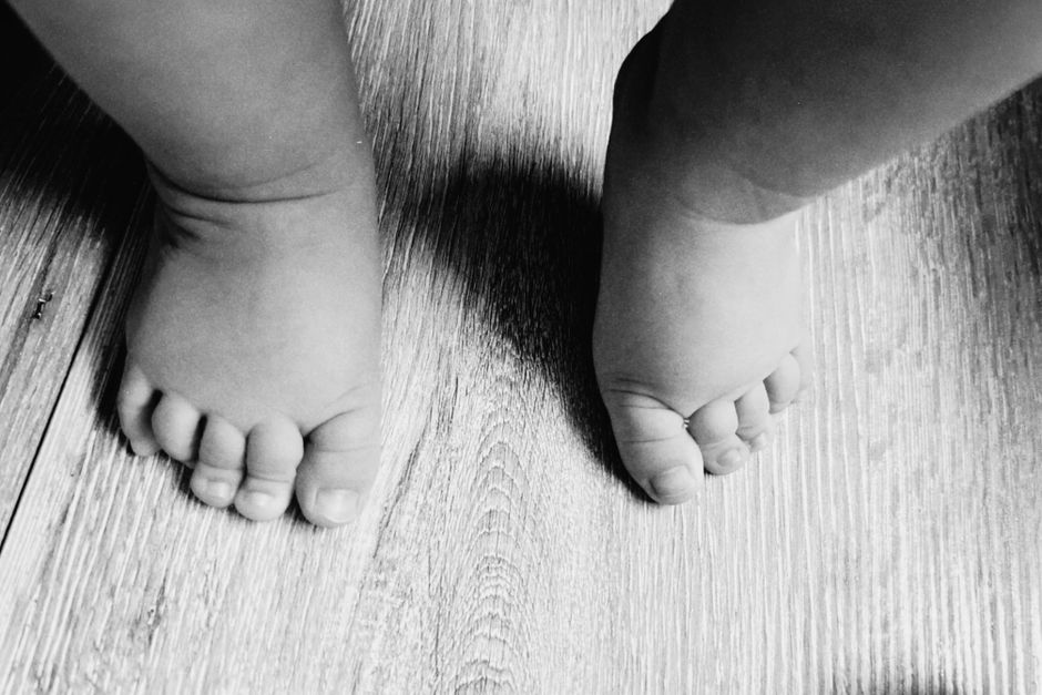 Adorable baby feet stepping on a wooden floor, captured in black and white