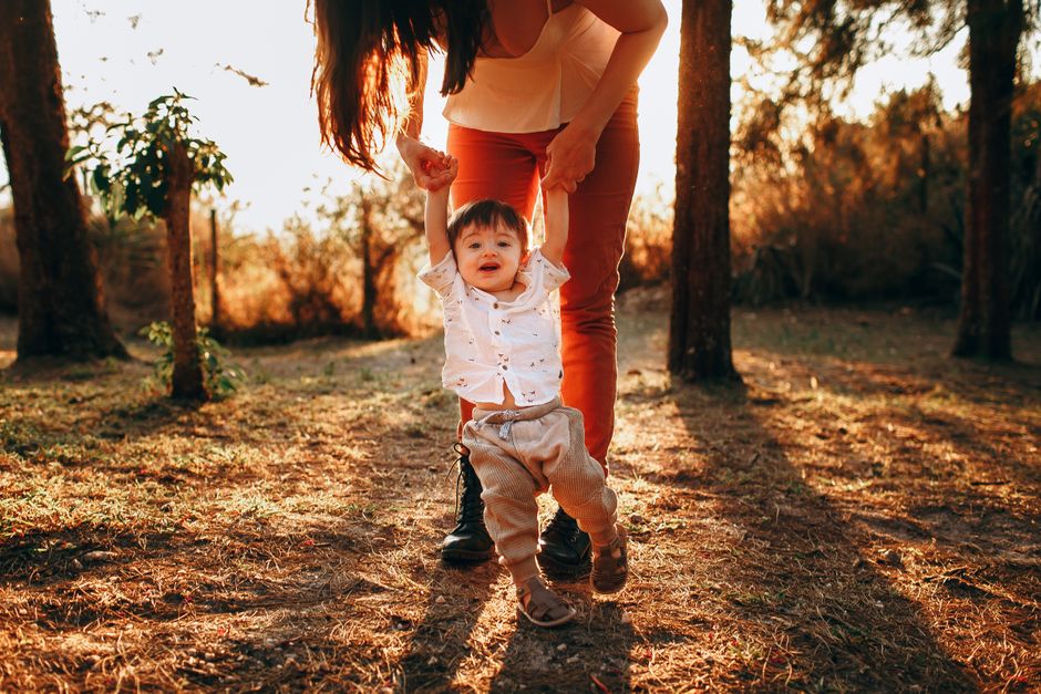 Mother helping her baby walk in a sunlit park, capturing a joyful moment