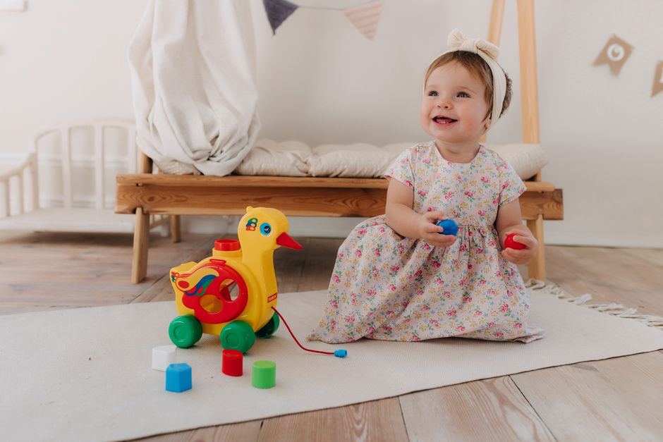 A cute baby boy happily lying on his tummy on a soft bed holding a toy during floor play